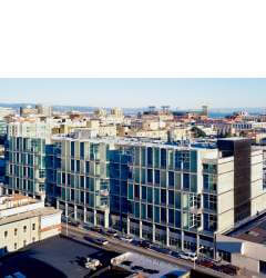 A view of low and medium height buildings stretching to the horizon. A harbor is visible in the far distance.