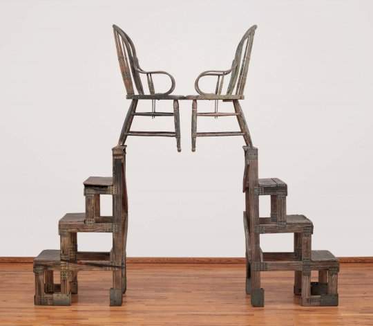 A sculpture made of two symmetrical wood and metal stands each with a wooden chair on top.