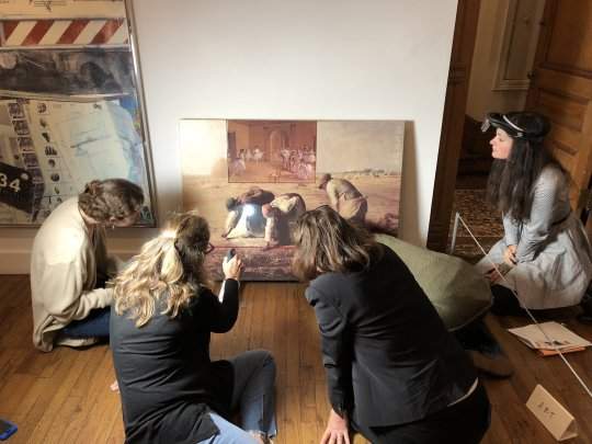 A group of five people sitting on the floor looking intently at an artwork depicting iconic paintings of Western art history. 