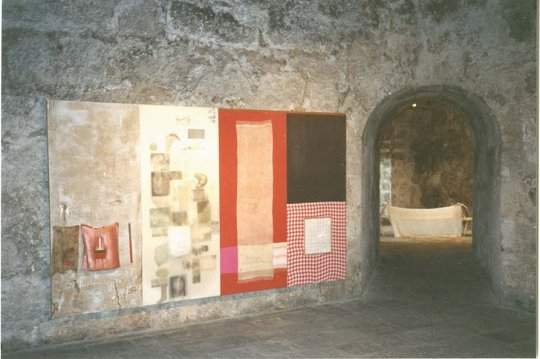 A large, colorful, four-panel artwork hangs on a stone wall, an arched doorway on the right leads to a room containing a white sculpture.