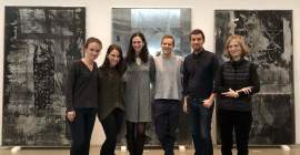 A group of six people wearing black, grey, and dark blue clothing, standing in front of three large artworks. The artworks contain black and grey silkscreened imagery on mirrored and brushed aluminum.