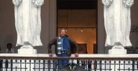 Robert Rauschenberg standing behind a balustrade, with two giant caryatids, columns carved in the shape of classical female figures, on either side of him.