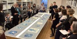 group of students and scholars gathered around table with square blueprints